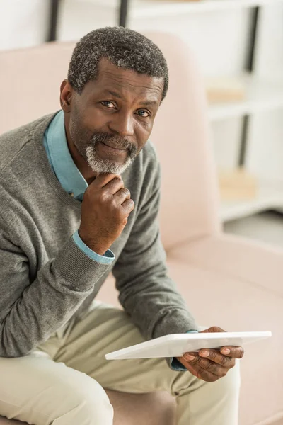 Americano africano pensivo segurando tablet digital enquanto olha para a câmera — Fotografia de Stock