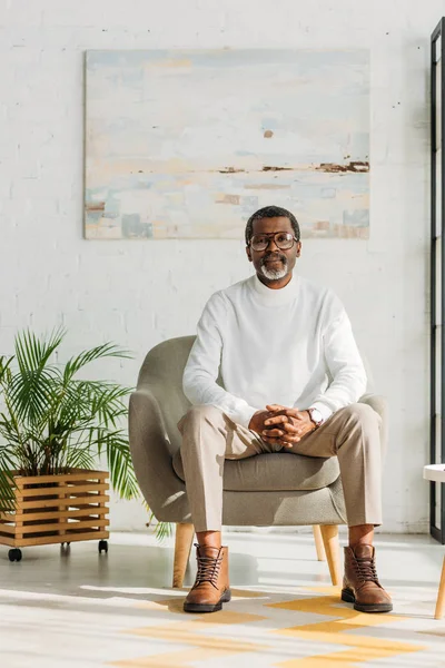 Stylischer afrikanisch-amerikanischer Mann sitzt im Sessel und blickt in die Kamera — Stockfoto