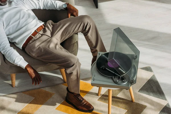 Vista cortada de homem americano africano elegante sentado em poltrona e ouvir música no gravador — Fotografia de Stock