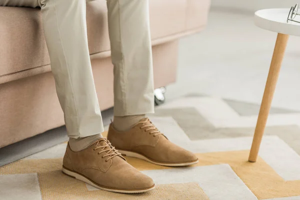 Vista cortada do homem em sapatos de couro elegantes sentados no sofá — Fotografia de Stock