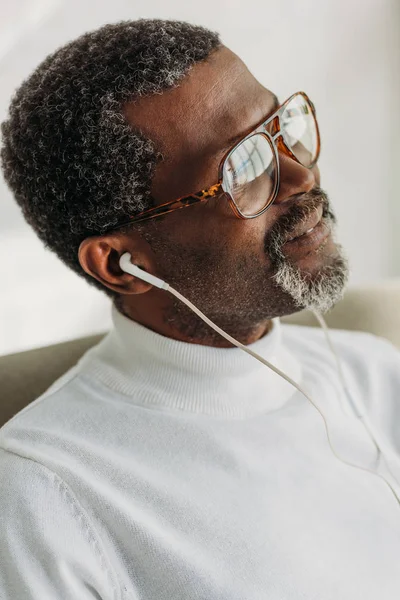 Dreamy african american man in glasses listening music in earphones — Stock Photo