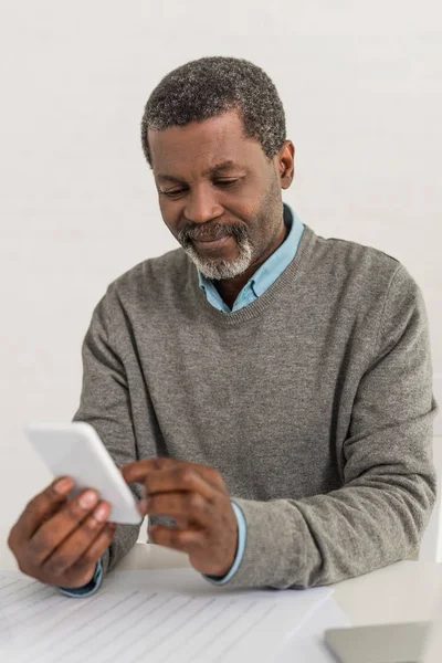 Älterer afrikanisch-amerikanischer Mann sitzt am Tisch und benutzt Smartphone — Stockfoto