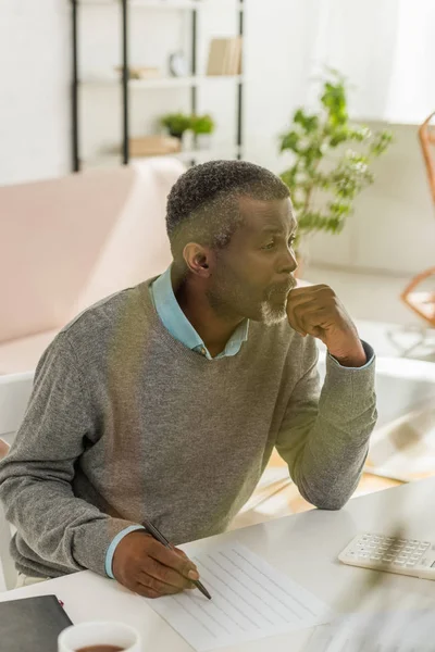 Homme afro-américain réfléchi assis à table près de facture de services publics et regardant loin — Photo de stock