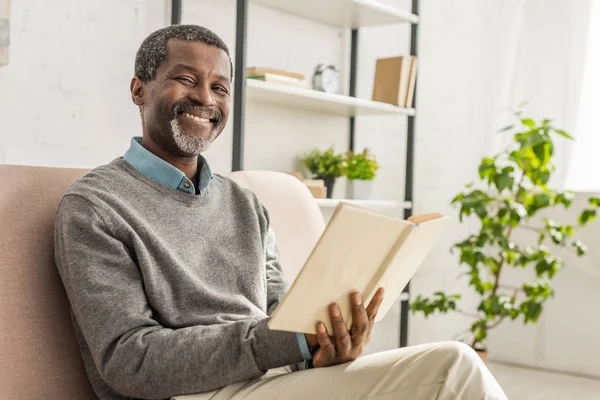 Homem americano africano alegre segurando livro e sorrindo para a câmera — Fotografia de Stock