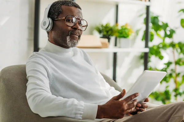 Élégant homme afro-américain tenant tablette numérique et écouter de la musique dans les écouteurs — Photo de stock