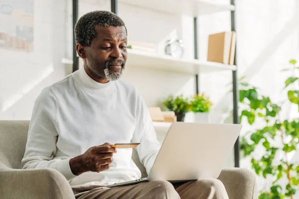 Älterer afrikanisch-amerikanischer Mann hält Kreditkarte während er Laptop benutzt — Stockfoto