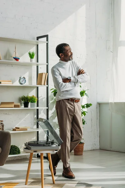 Stylish african american man standing with crossed arms while listening music on record player — Stock Photo