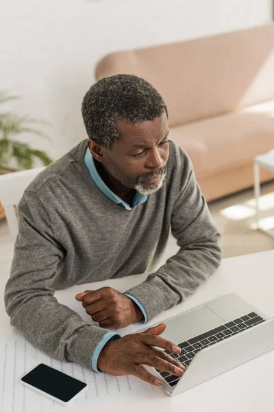 Ernster afrikanisch-amerikanischer Mann sitzt am Tisch und benutzt Laptop — Stockfoto
