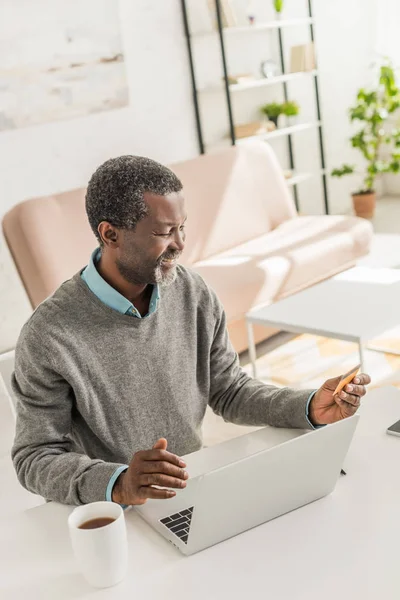 Allegro uomo africano americano seduto vicino al computer portatile e in possesso di carta di credito — Foto stock