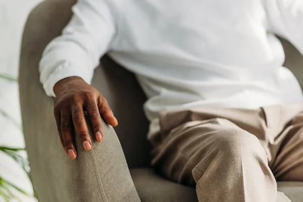 Recortado vista de mayor afican americano hombre sentado en sillón - foto de stock