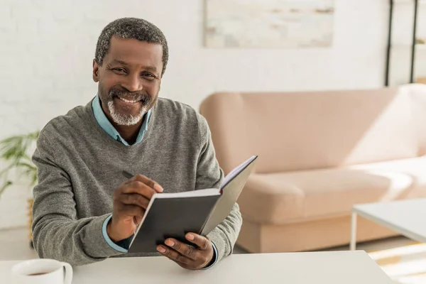 Allegro uomo africano americano sorridente alla macchina fotografica mentre tiene il notebook — Foto stock