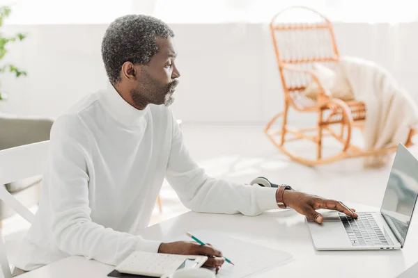 Serious african american man using laptop while calculating communal expenses — Stock Photo