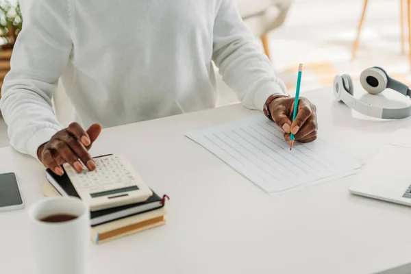 Vue recadrée de l'homme afro-américain écrivant dans la facture de services publics et le calcul des dépenses — Photo de stock