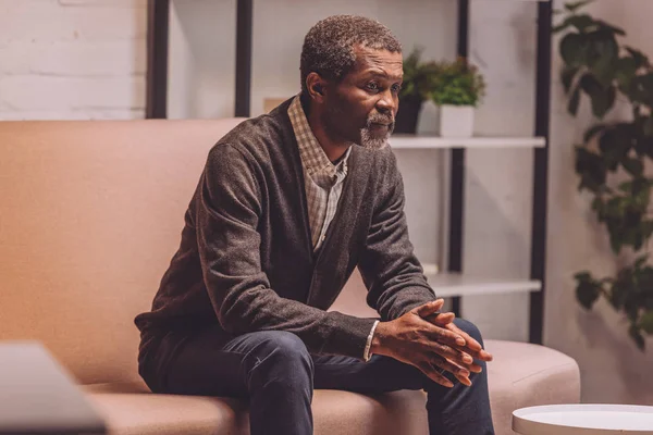 Homme afro-américain déprimé assis sur le canapé la nuit — Photo de stock