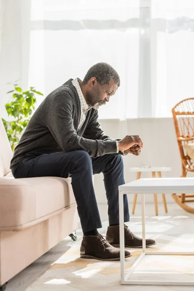 Homme afro-américain déprimé assis sur un canapé avec la tête inclinée — Photo de stock