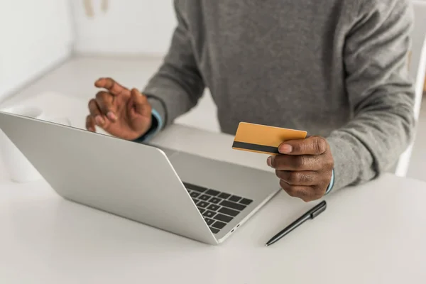 Vista ritagliata di uomo africano americano in possesso di carta di credito durante l'utilizzo del computer portatile — Foto stock