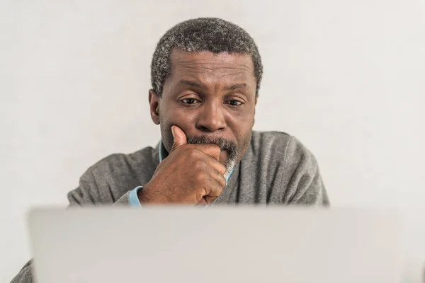Enfoque selectivo del hombre afroamericano reflexivo sentado cerca de la computadora portátil - foto de stock