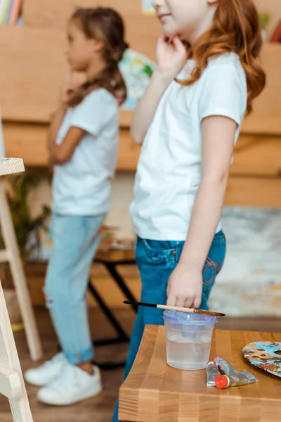 Обрезанный вид на детей, стоящих возле деревянного стола с гуашью красками — стоковое фото