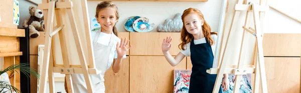 Panoramic shot of happy kids waving hands in art school — Stock Photo