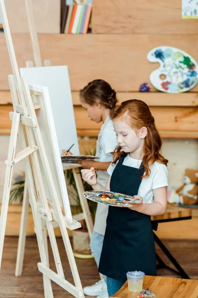 Niedliche Kinder mit Palette und Malerei in der Kunstschule — Stockfoto