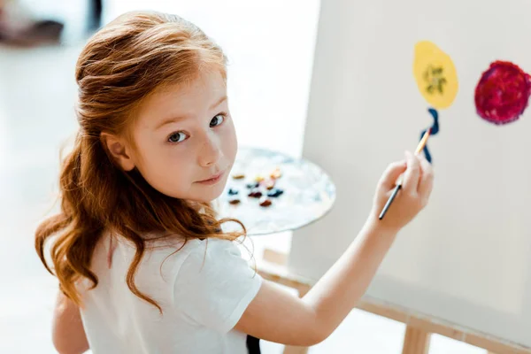 Selective focus of cute redhead kid painting in art school — Stock Photo