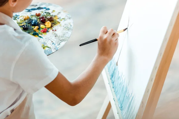Vista recortada de niño jadeando sobre lienzo en la escuela de arte - foto de stock