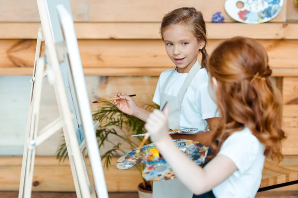 Селективное внимание милого ребенка, смотрящего на рыжего ребенка в художественной школе — стоковое фото