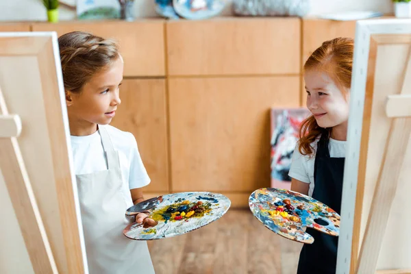 Messa a fuoco selettiva di bambini che tengono tavolozza colorata e si guardano l'un l'altro — Foto stock