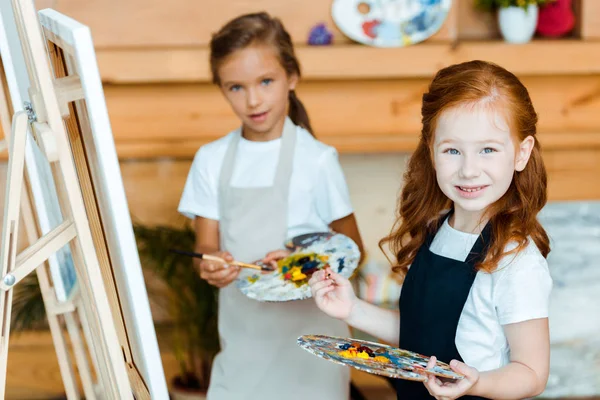 Enfoque selectivo de niña pelirroja feliz sonriendo cerca de niño con paleta - foto de stock