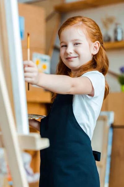 Selective focus of positive redhead child holding paintbrush — Stock Photo