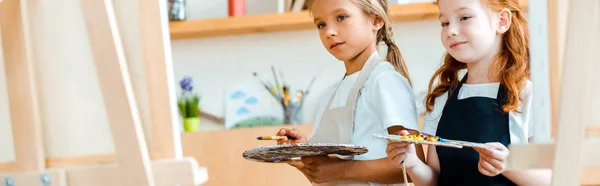 Panoramic shot of kids with paintbrushes near canvas — Stock Photo