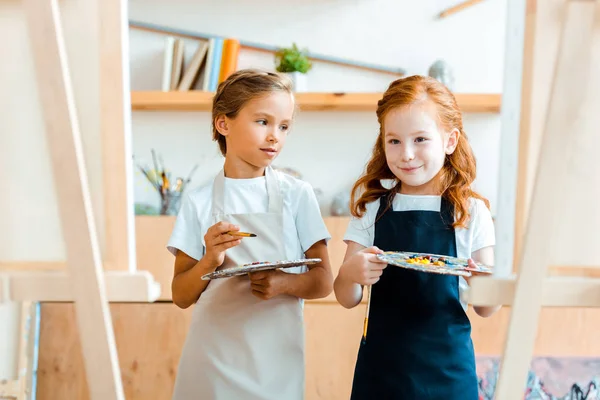 Foyer sélectif des enfants heureux avec palette multicolore près de la toile — Photo de stock