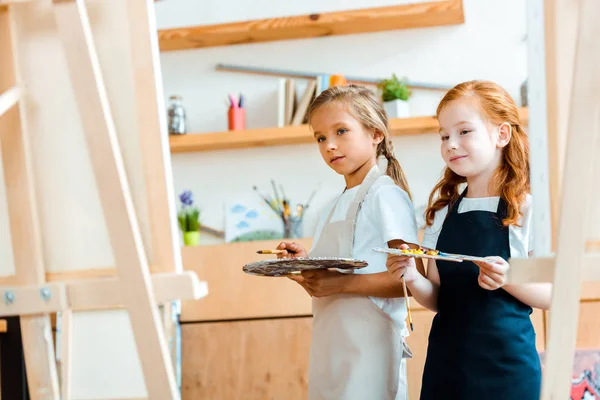 Focus selettivo di bambini allegri con tavolozza multicolore vicino alla tela — Foto stock