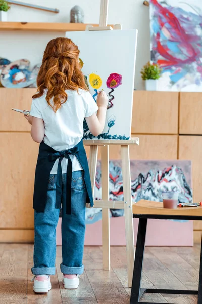 Back view of redhead kid painting on canvas — Stock Photo