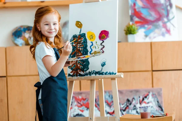 Happy redhead kid painting on canvas in art school — Stock Photo