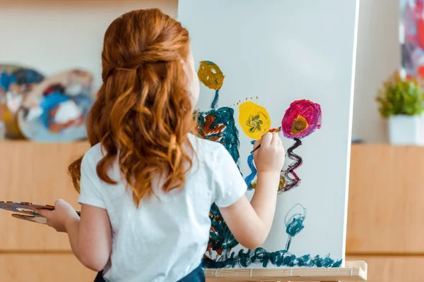 Back view of redhead child painting on canvas in art school — Stock Photo