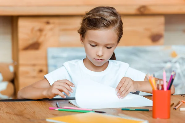 Selective focus of kid looking at paper near color pencils on table — Stock Photo