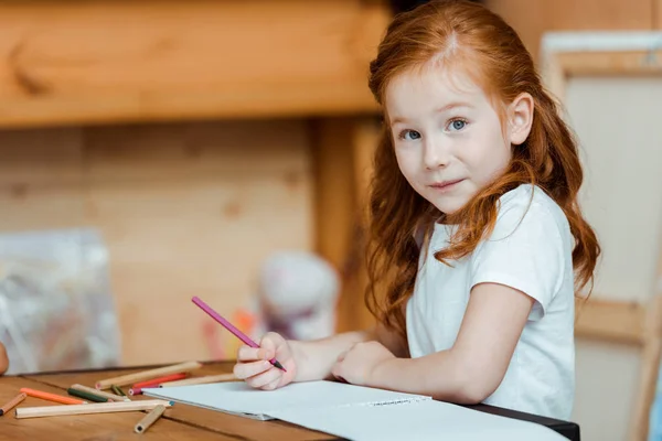 Mignon rousse enfant tenant crayon de couleur et regardant caméra — Photo de stock