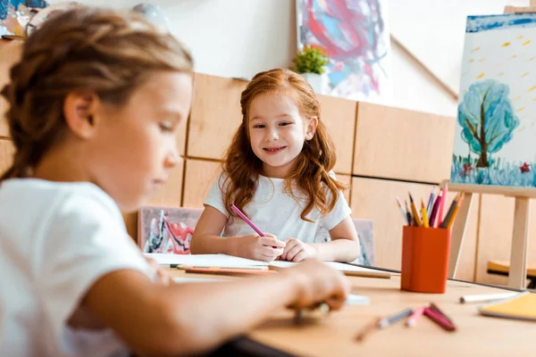 Selective focus of happy redhead kid with color pencil looking at child — Stock Photo