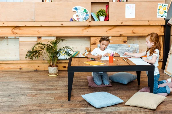 Cute kids sitting on pillows and drawing at desk — Stock Photo