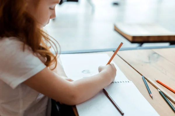 Selective focus of redhead kid drawing on paper with color pencil — Stock Photo