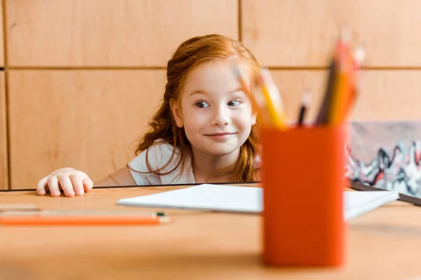 Foyer sélectif de sourire rousse enfant près des crayons de couleur sur la table — Photo de stock