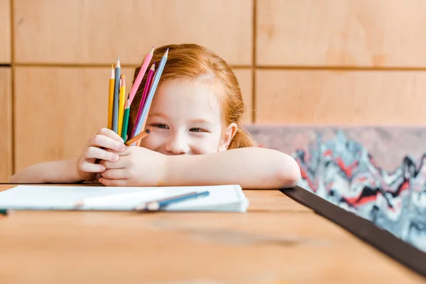 Messa a fuoco selettiva di bambino rossa sorridente che tiene matite di colore — Foto stock