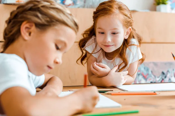 Messa a fuoco selettiva di cute rossa bambino guardando adorabile bambino disegno su carta — Foto stock