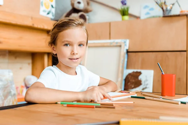 Избирательный фокус счастливого ребенка, улыбающегося и смотрящего на камеру в художественной школе — стоковое фото