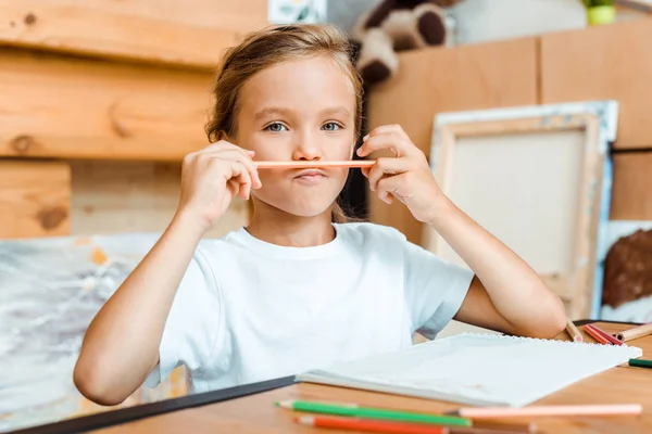 Foco seletivo de criança bonito segurando lápis de cor perto do rosto — Fotografia de Stock