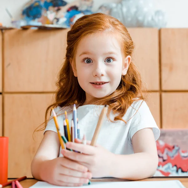 Cute and excited redhead kid holding color pencils in art school — Stock Photo