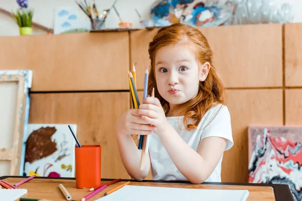 Милый рыжий ребенок держит цветные карандаши в школе искусств — стоковое фото