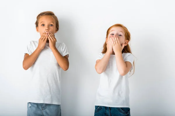 Simpatici bambini in piedi e volti di copertura su bianco — Foto stock