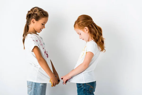 Vista lateral de crianças alegres com tinta em camisetas em pé no branco — Fotografia de Stock